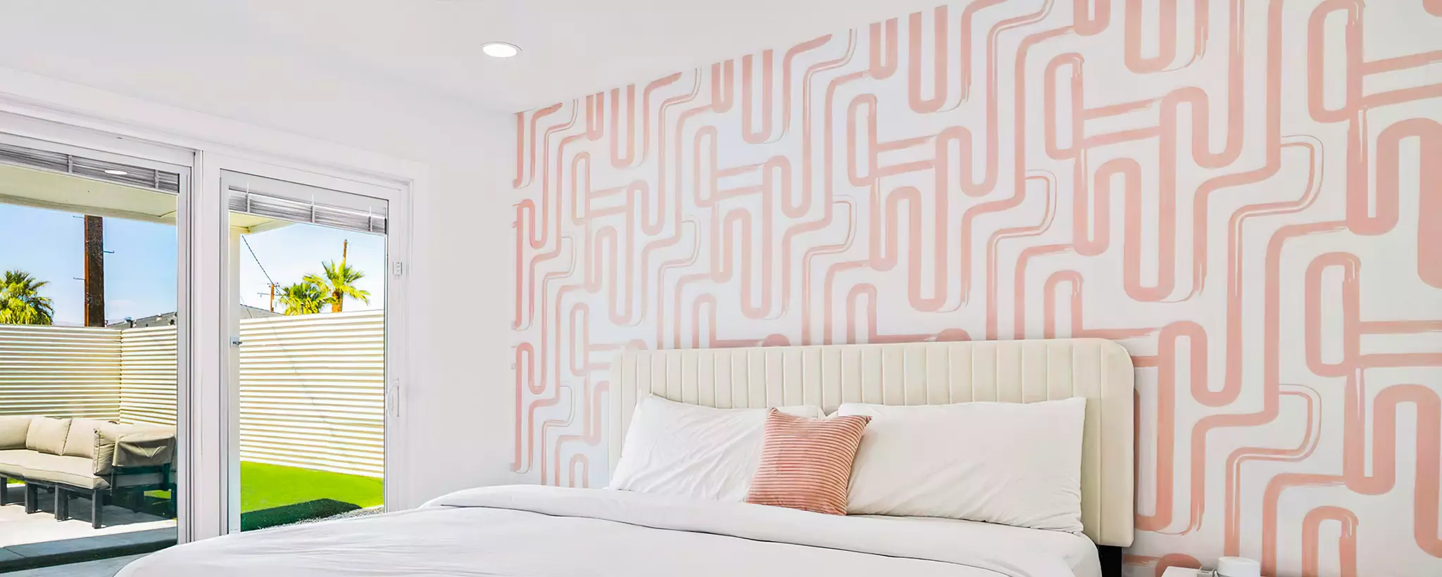 Modern bedroom with geometric patterned wall, bed, and outdoor view. Desktop slider.