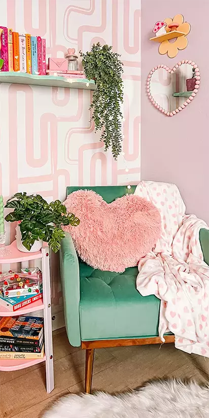 Pink heart-shaped pillow on a green chair in a room with patterned walls and shelves. Mobile slider.